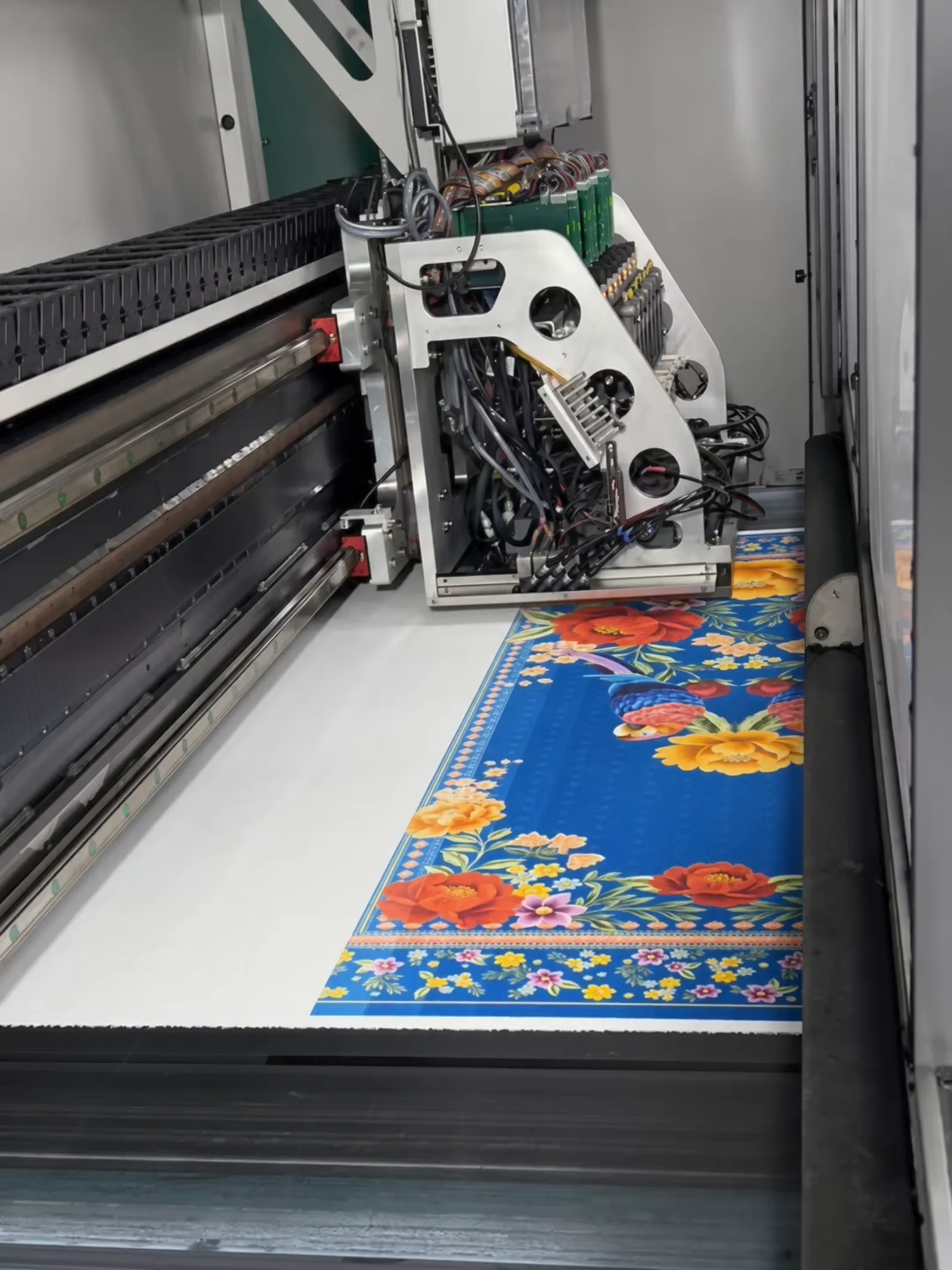 Impressora digital de grande formato estampando um tecido floral sobre fundo azul.